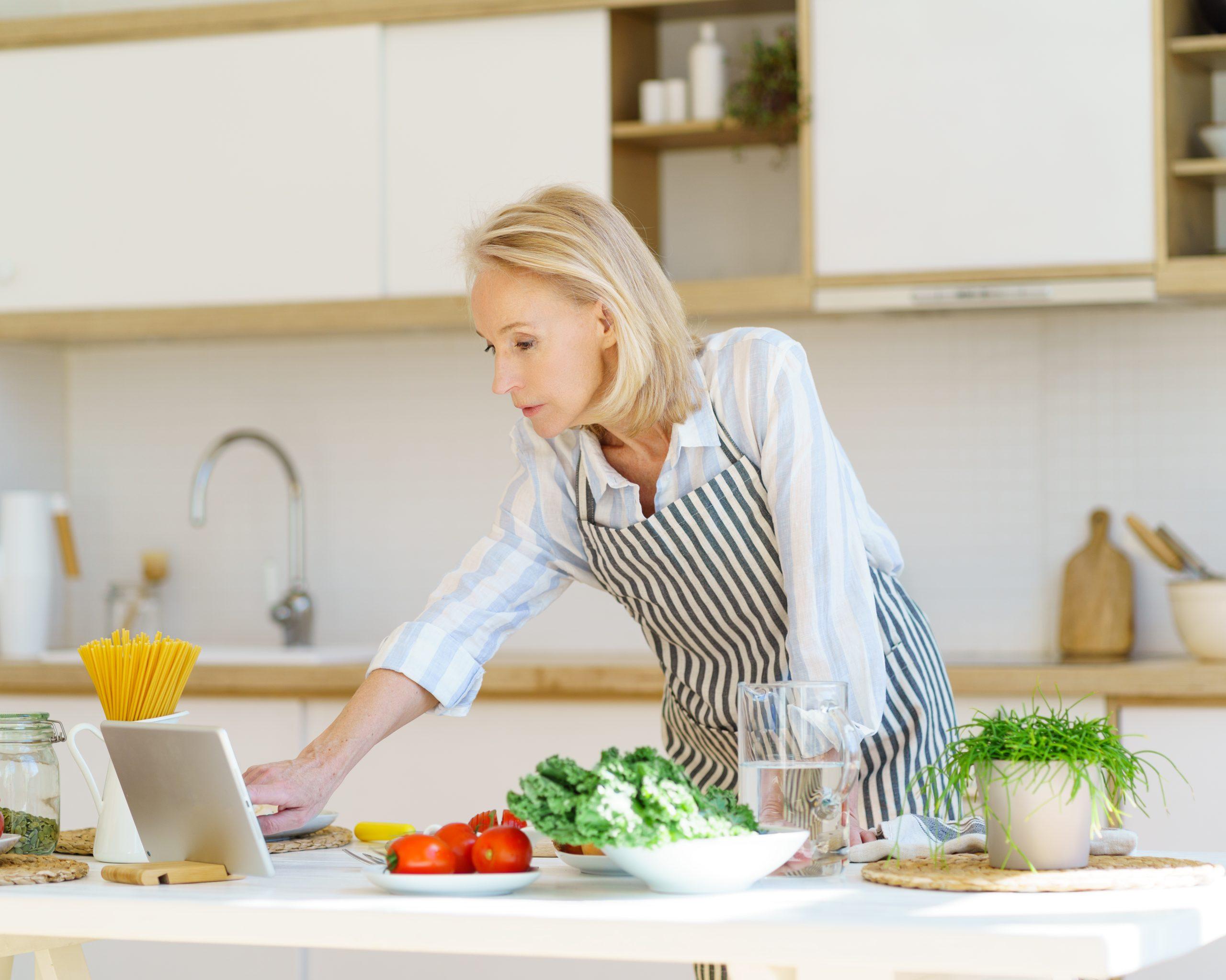 Senior woman watching video recipe on digital tablet while cooking on retirement at home